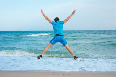 Kaldırılmış elleri ve bacakları olan mutlu adam denize atlıyor, geriye bakıyor.