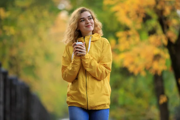 黄色のジャケットの女性は秋の日に路地を歩く熱いお茶を飲む — ストック写真