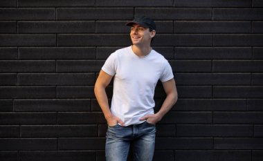 Tuğla duvarın önünde duran beyaz tişörtlü, gülümseyen adam, model şablon.