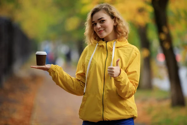 黄色のジャケットの女性は秋の日にテイクアウトコーヒーを実証 — ストック写真