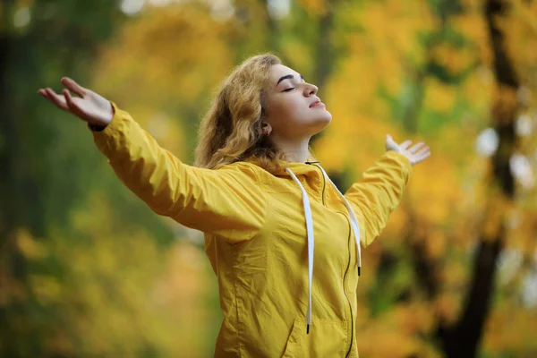 立ち上がり手で黄色のジャケットの女性は秋の日に呼吸空気を楽しむ — ストック写真