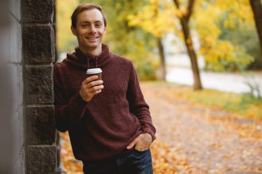 Adam sonbahar günü sokakta yürürken sıcak çay içer.