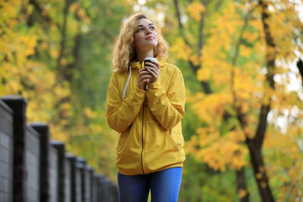黄色のジャケットの女性は秋の日に路地を歩く熱いお茶を飲む — ストック写真