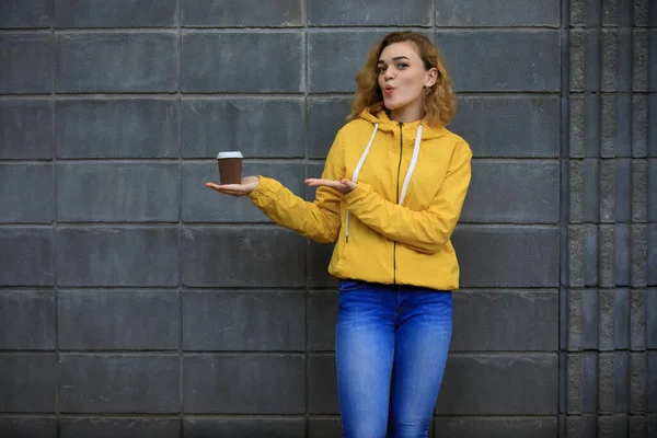 Donna Giacca Gialla Dimostrano Caffè Asporto Vicino Alla Parete Grigia — Foto Stock