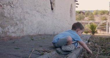 Little boy sitting outside near wall and playing with stick