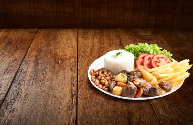 Tahta arka planda pirinçli, fasulyeli, salatalı, patates kızartmalı kıyma.