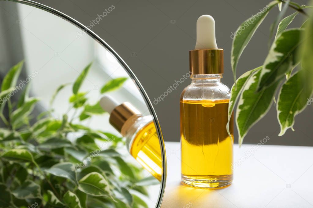 Oil serum in glass bottle with pipette. Yellow essence on gray background