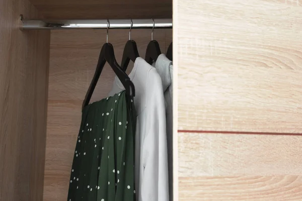 Open wooden wardrobe closet with clothes on black hanger