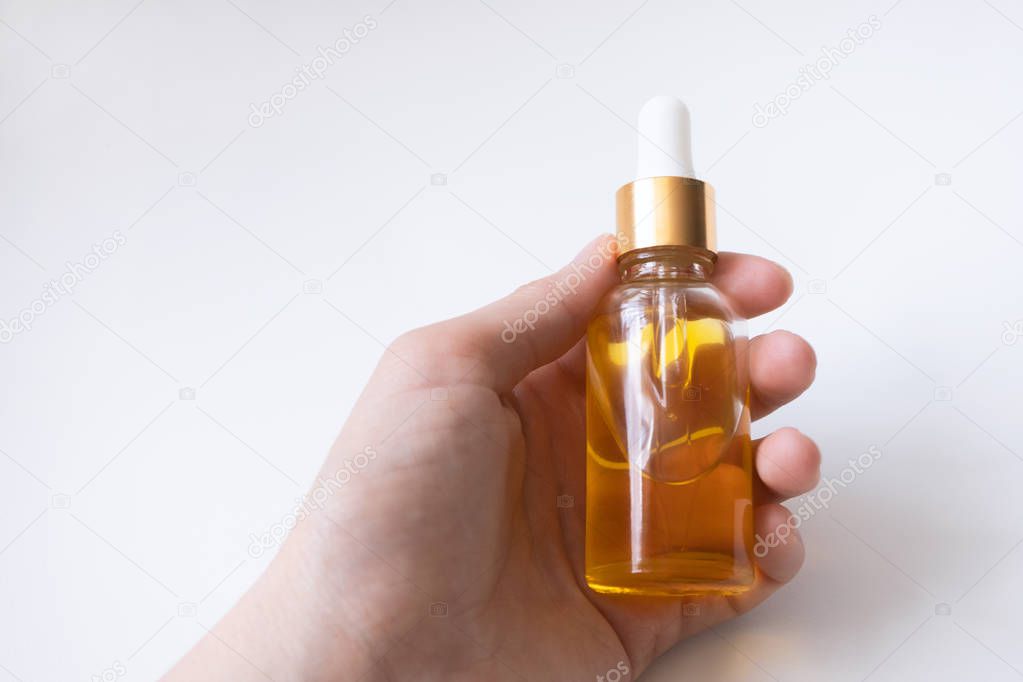 Woman hand holding glass bottle with oil serum