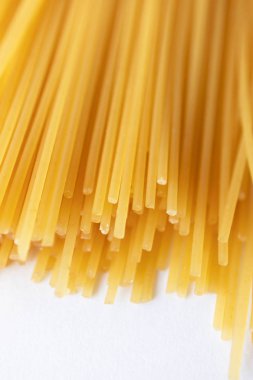 Beyaz arka planda izole İtalyan sarı spagetti yığını. Seçici odaklı makarna dokusu, yakın çekim. Gıda dikey fotoğraf