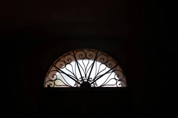Semicircular window with a decorative grate on a dark background — Stock Photo, Image