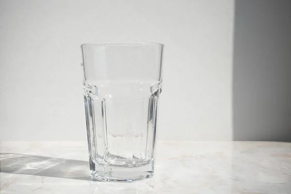 Άδειο γυαλί σε ένα τραπέζι μπροστά από τον λευκό τοίχο με σκιά — Φωτογραφία Αρχείου