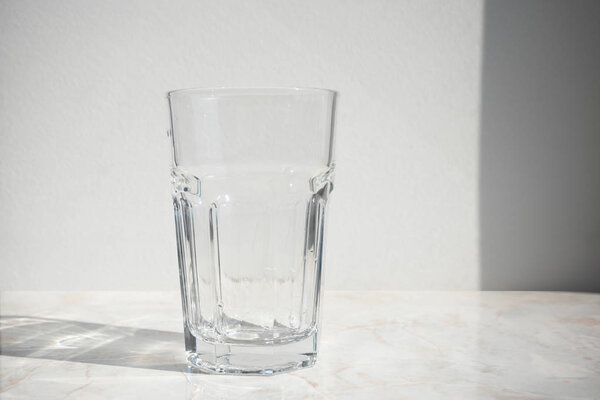 Empty glass on a table in front of white wall with shadow