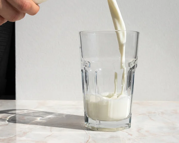 Leche de la botella que vierte en el vidrio que permanece en la mesa ligera —  Fotos de Stock