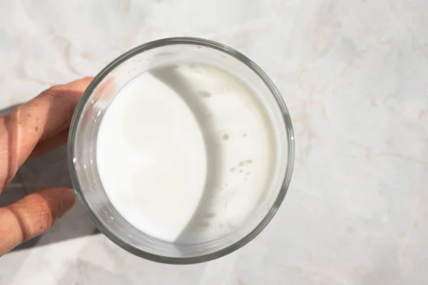 Mano sostiene el vaso de leche cruda de pie sobre la mesa de mármol ligero —  Fotos de Stock