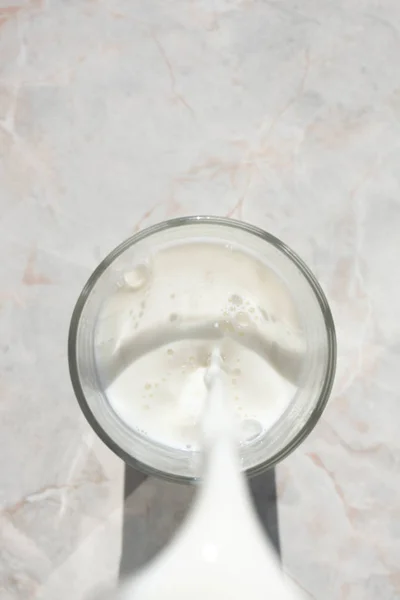 Flowing milk. Close-up of milk stream pouring into glass, top vi — Stock Photo, Image