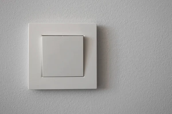 White plastic light switch on light gray wall, close-up. Copy sp