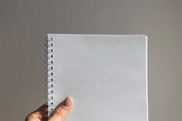 Weibliche Hand hält offenen Notizblock mit leerem Blatt auf grauer Wandrückseite — Stockfoto