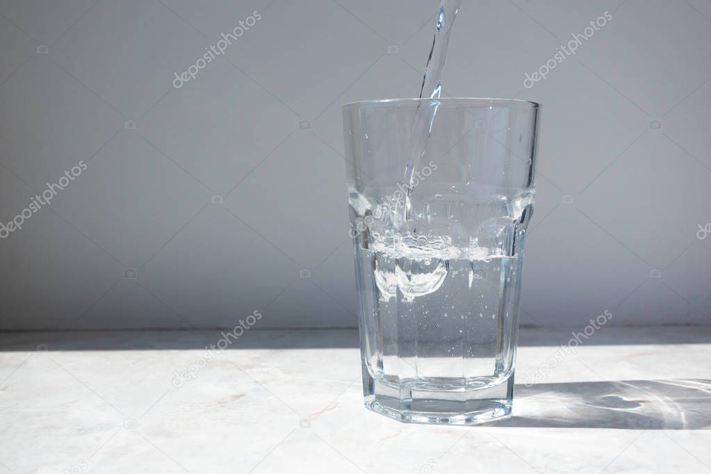 Mineral water pouring into glass on white stone table