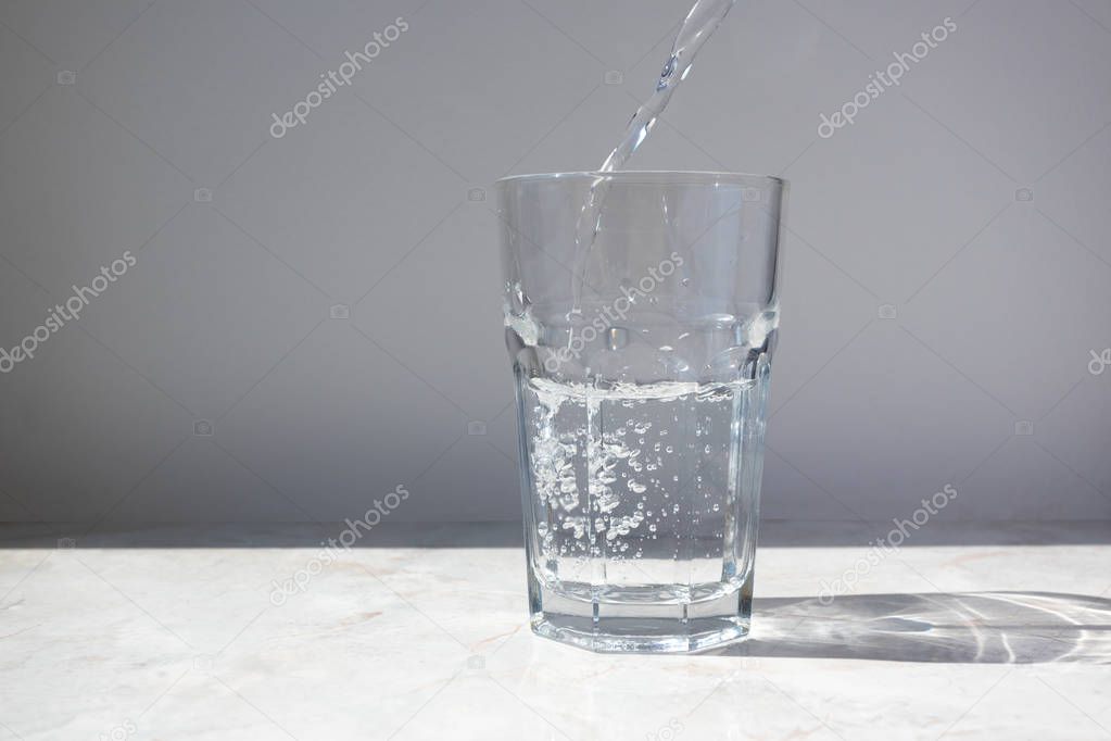 Clear water puring into glass on white wall background
