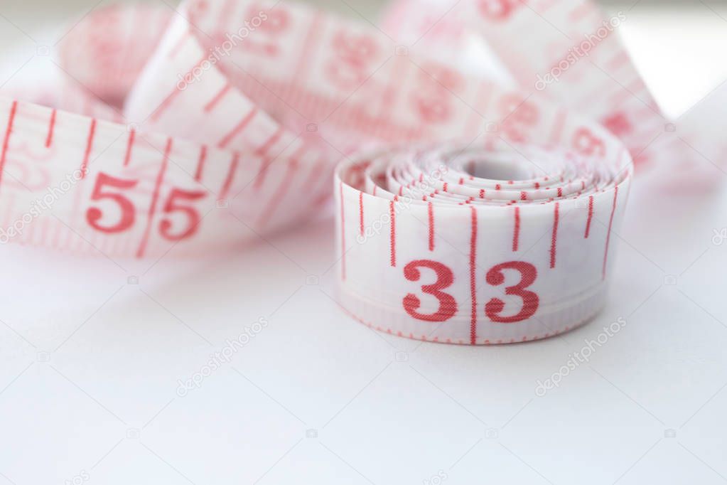 Close-up cloth tape measure with red numbers rolled up on white 