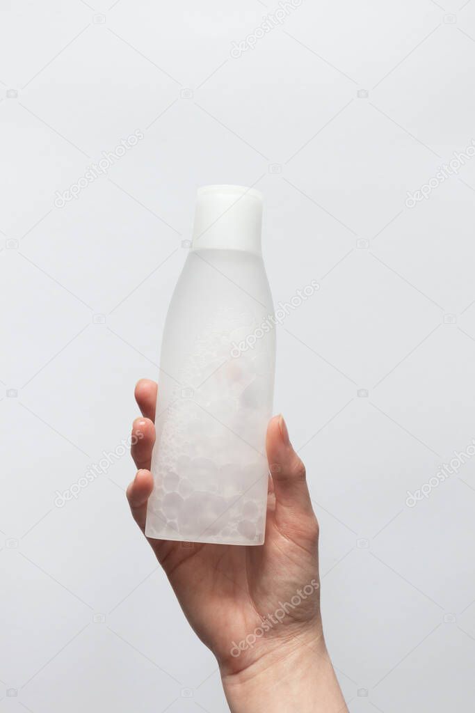 Girl holding in hand toner or tonic bottle for skincare on white background. Facial skin care beauty product, vertical