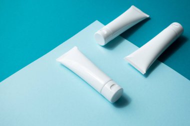 Nemlendirici el kremi beyaz plastik tüpler mavi modaya uygun kağıt arka plan, izometrik. Boş cilt bakımı güzellik ürünleri paketleme