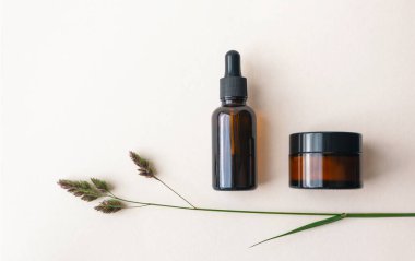 Kahverengi cam şişede göz nemlendirici krem ve serum ve açık bej arka planda çayır otu. Cilt bakımı için ekolojik organik doğal kozmetik ürünleri kavramı