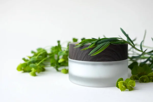 Nemlendirici yüz kremi ya da buzlu cam kavanozda, ahşap bardak, çayır otları ve bej arka planda yapraklarla birlikte göz kremi. Çevresel doğal organik cilt bakımı ve vücut bakımı ürünleri.