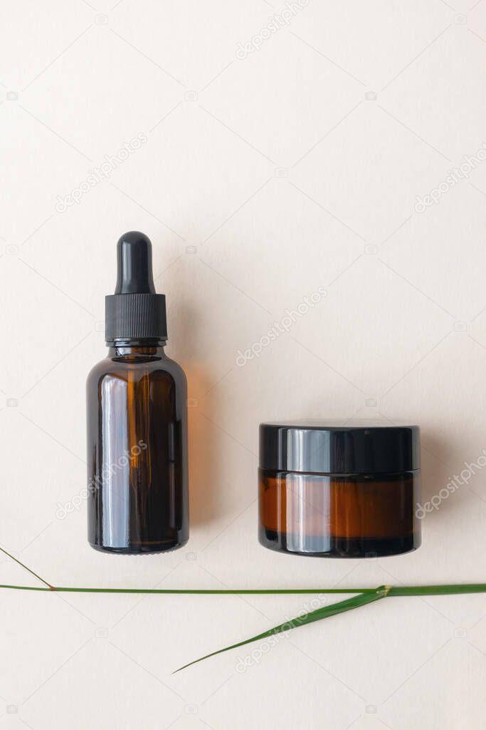 Moisturizer cream and serum in brown glass bottle and jar on light beige background, top view. Concept eco organic natural cosmetic products for skincare, vertical
