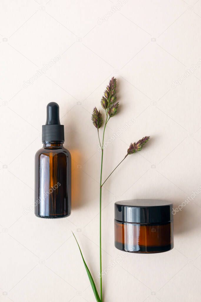 Mockup moisturizer cream and serum in brown glass bottle and jar and meadow herb on light beige background, above. Concept eco organic natural cosmetic products for skincare, vertical