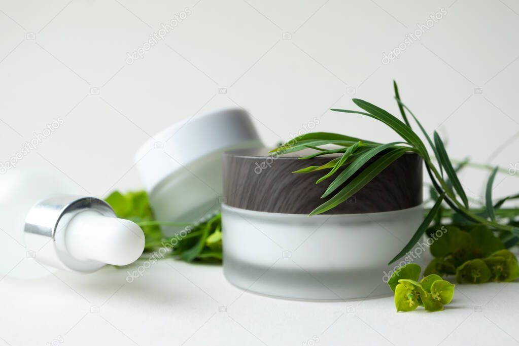 Concept eco natural organic skincare and bodycare beauty products with selective focus. Moisturizer facial or eye cream in frosted glass jar with wooden cup and herbs on beige background