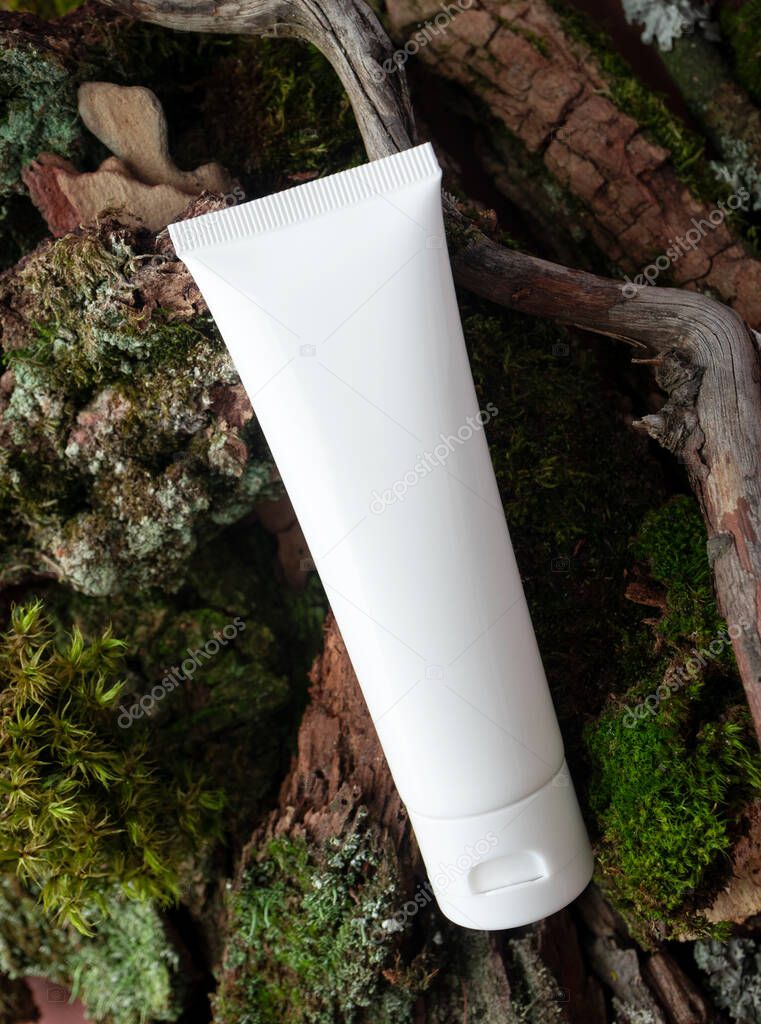 Close-up white hand cream, body lotion or facial cleanser tube mockup on moss, tree bark and branch, top view. Bio organic beauty product for skin and body care with natural extract in forest