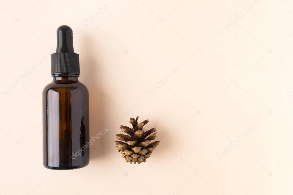 Serum bottle from brown glass with pipette and pine cone on beige background with copy space. Concept bio organic beauty product with natural extract flat lay. Eco cosmetic skincare and body care