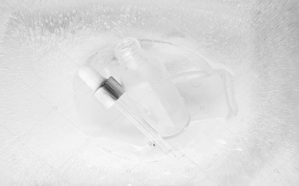 Pipette from serum bottle from frosted white glass in ice background and selective focus. Concept summertime beauty product, above. Cooling moisturizer fluid