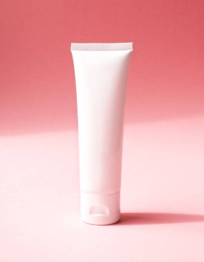 Kozmetik ürünler için tek bir beyaz plastik tüp yakın çekim, ön görüş. El kremi için konteyner, nemlendirici vücut losyonu, yüz temizleyici veya pembe arka planda çapraz gölgeli şampuan.