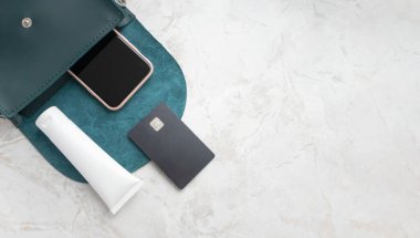 Beyaz tüp krem, kredi kartı ve akıllı telefon. Küçük bir kadın çantasında. Fotokopi alanı olan lüks mermer arka planda. Masa üstü modeli moda ve güzellik konsepti. E-ticaret cilt bakım ürünleri düz yatıyordu