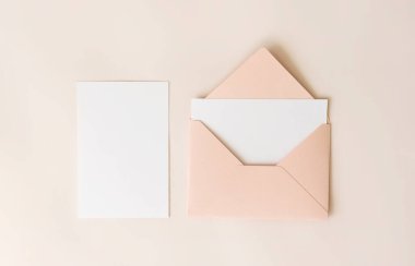 Pembe zarfın içindeki boş harf ve bej arka plan beyaz kağıt, üst manzara. Tebrik kartı konsepti. Düğün davetiyesi şablonu