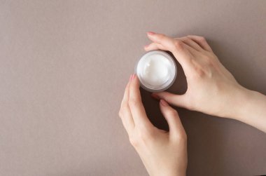 Cam kavanozdaki krem nemlendirici kadının ellerinde bej arka plan ve fotokopi alanı. Güzellik cilt konsepti