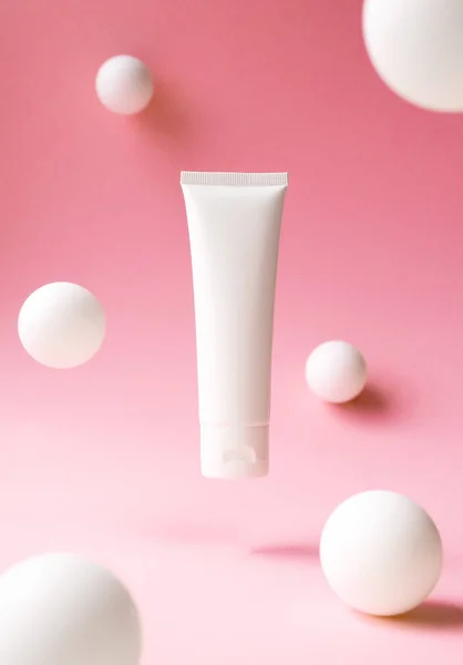 Pembe arka planda kozmetik ürün için beyaz plastik tüp, soyut beyaz küreler, ön görüş. El kremi için kap, nemlendirici vücut losyonu, yüz temizleyici veya şampuan, dikey