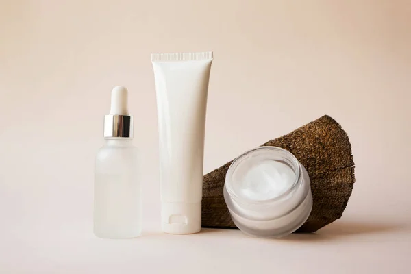 Serum dropper, body lotion on tube and open moisturizer cream in white glass jar and textured defocused wooden tree cut surface on beige background. Concept branding natural cosmetic products set