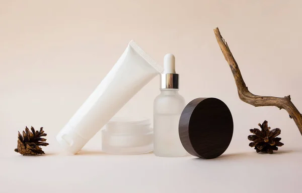 Balancing body lotion in white plastic tube, open moisturizer cream, liquid serum, pine cones and tree branch on beige background, front view. Branding beauty cosmetic products collection mockup