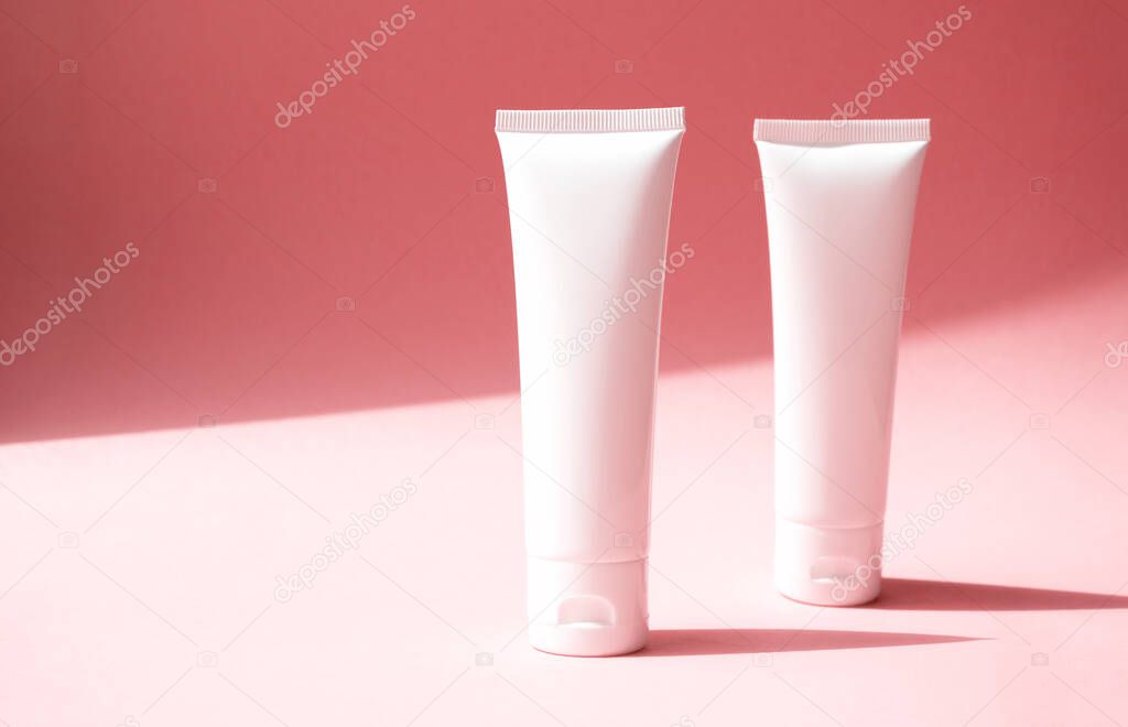 Mockup two white plastic tubes for cosmetic products. Container for hand cream, moisturizer body lotion, facial cleanser or shampoo on pink background with diagonal shade on backdrop, front view