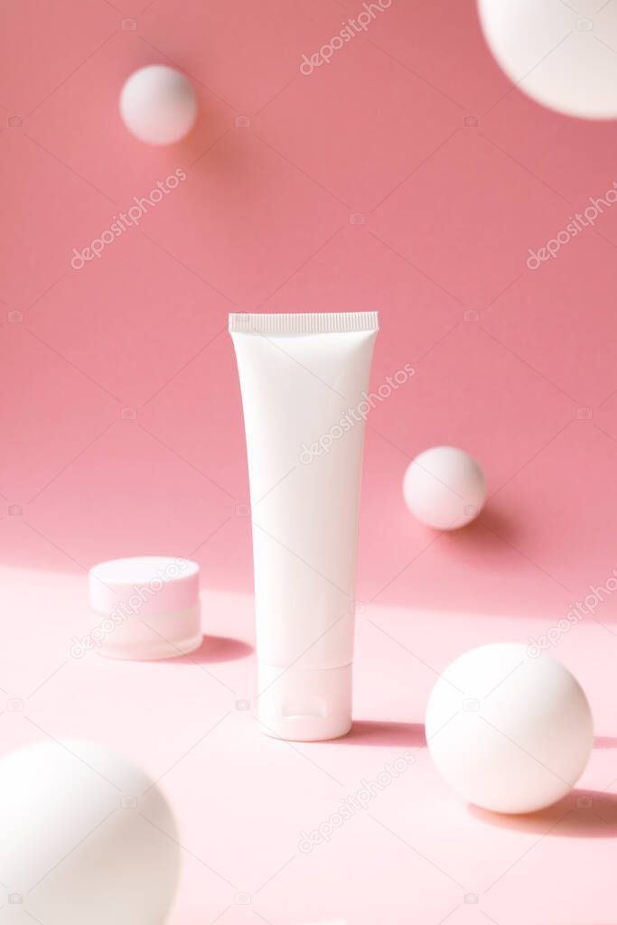 White plastic tube for cosmetic product on pink background with abstract white spheres, front view. Containers for eye moisturizer, hand cream, body lotion, facial cleanser or shampoo, vertical