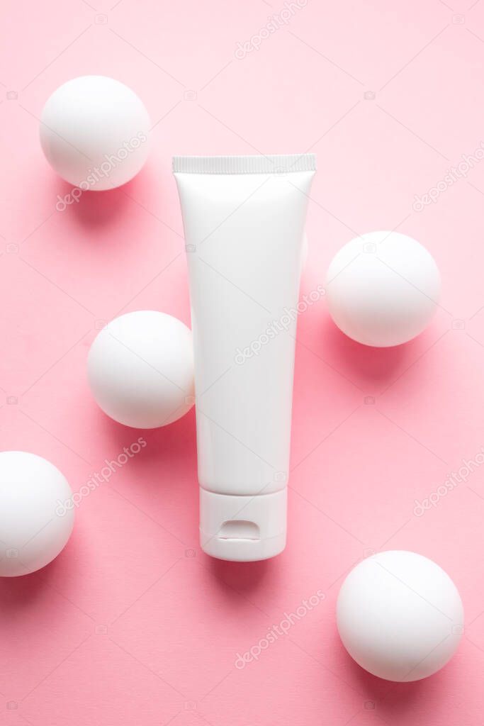Moisturizer cream tube on creative pink background with white ping pong balls. Abstract beauty product photo with geometric sphere shapes. Concept delicacy, lightness and pure skincare, vertical