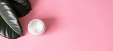 Pembe arka planda nemlendirici krem, fotokopi alanı ve yeşil tropikal yapraklar, üst manzara. Eko doğal organik özüt deri bakımı konsepti. Dermatoloji ve kozmetoloji minimalist düz yatıyordu