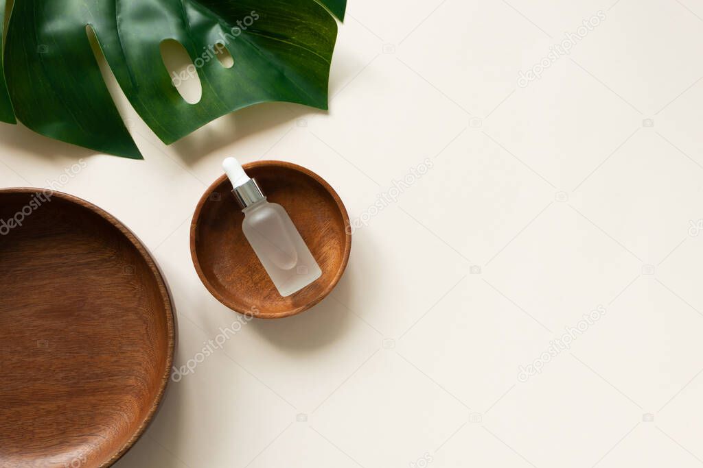 Essential serum in wooden plate and monstera leaf flat lay composition on light beige background with copy space, top view. Concept organic natural vegan cosmetic beauty product