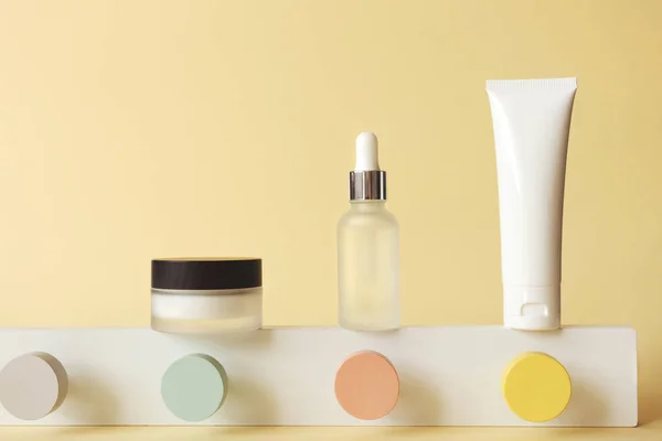Tüp, şişe ve kavanoz cilt ürünleri. Geometrik soyut podyumda duran pastel sarı arka planda.