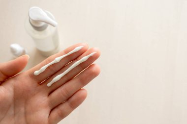 Close-up of female hand with sunscreen cream stripes on two fingers, illustrating the two-finger rule for proper SPF application