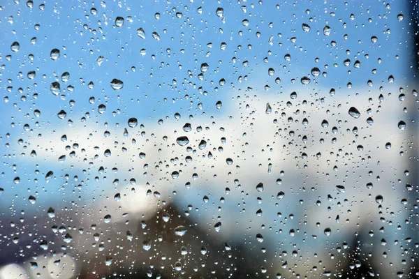 Raindrops on the transparent window pane. Background of raindrops on a wet, gray and opaque glass texture. Outside the window, rainy summer weather. Blurred background, urban landscape.